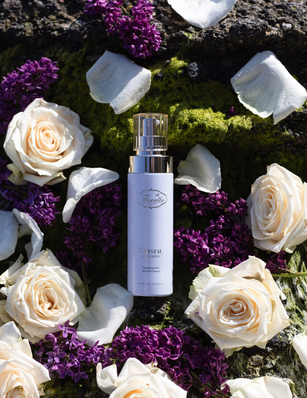 Floralla Crystal Moisturizing Essence packaging with hydrating anti-wrinkle formula, displayed among white roses and purple lilacs on a green moss background, representing natural skincare and beauty.