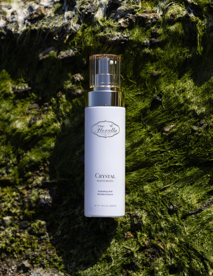 Floralla Crystal Moisturizing Essence packaging with hydrating anti-wrinkle formula, displayed on a green moss background, representing natural skincare and beauty.