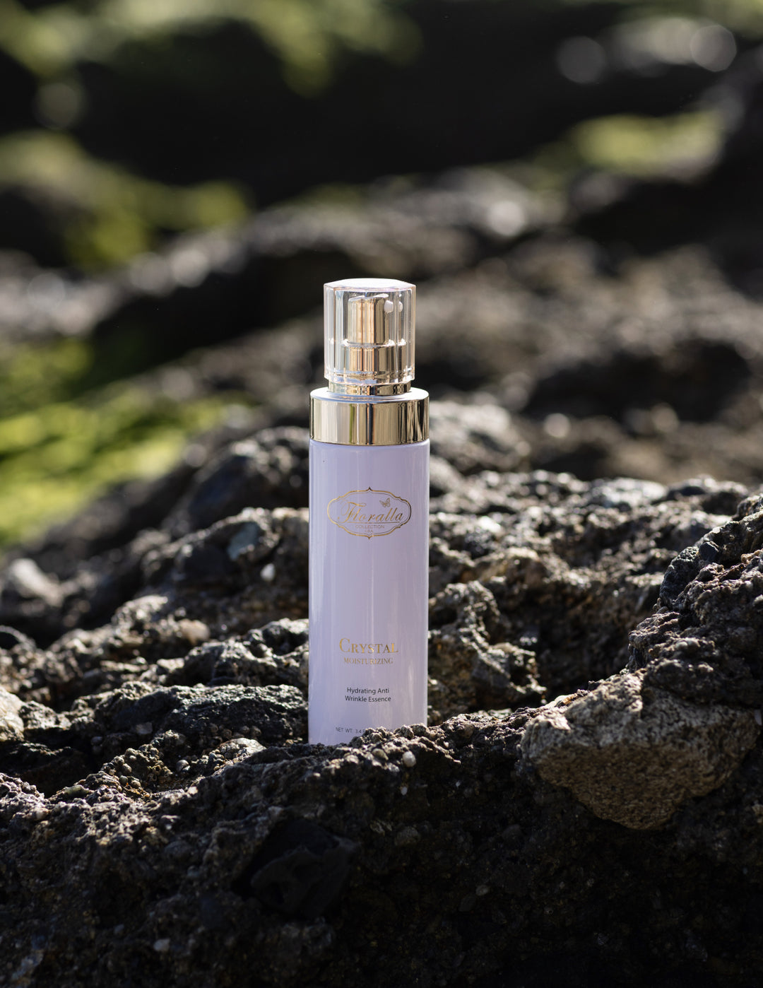 Floralla Crystal Moisturizing Essence packaging with hydrating anti-wrinkle formula, displayed among white roses and purple lilacs on a rock background, representing natural skincare and beauty.